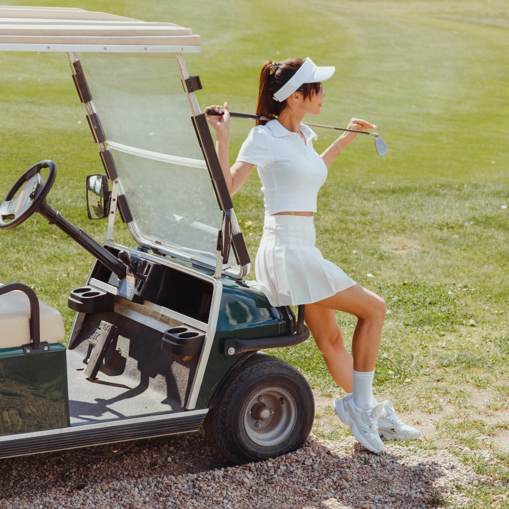 Beautiful woman in white outfit standing near golf cart. Rich lifestyle