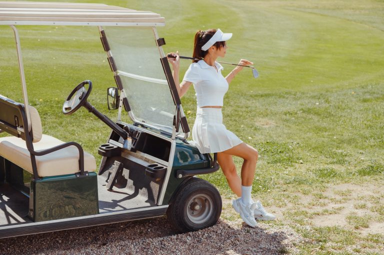 Beautiful woman in white outfit standing near golf cart. Rich lifestyle