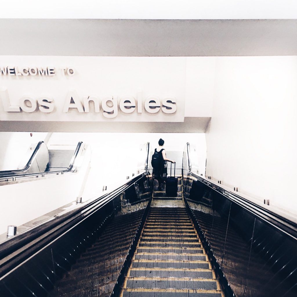 A person with a luggage going down an escalator with a sign WELCOME TO LOS ANGELES up above