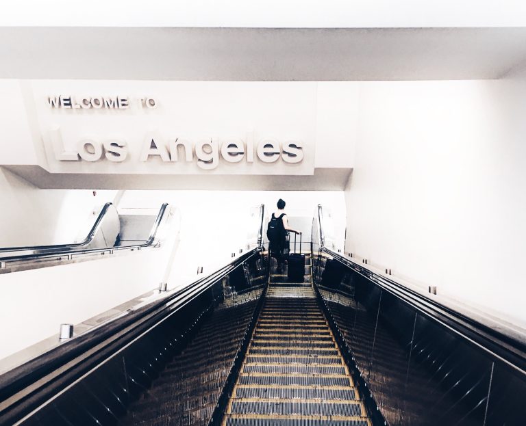 A person with a luggage going down an escalator with a sign WELCOME TO LOS ANGELES up above