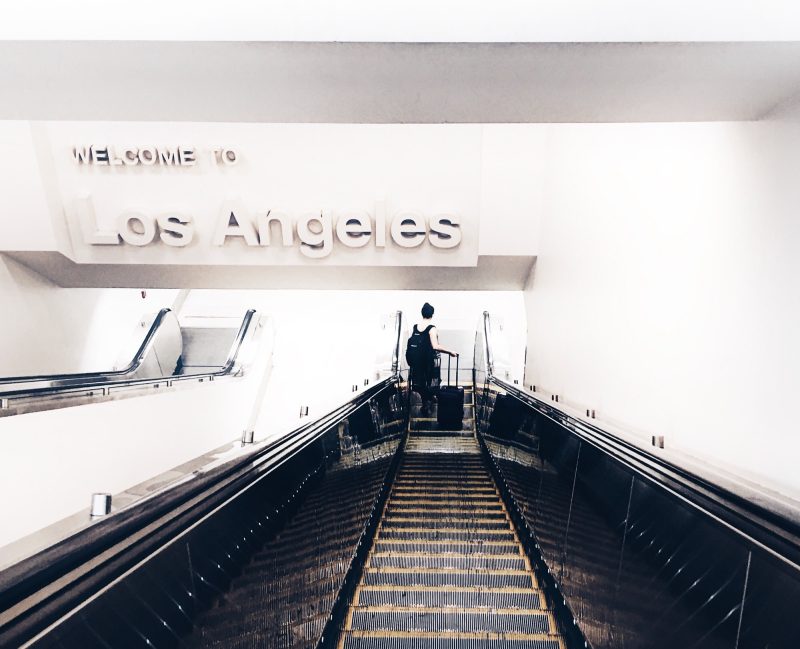 A person with a luggage going down an escalator with a sign WELCOME TO LOS ANGELES up above